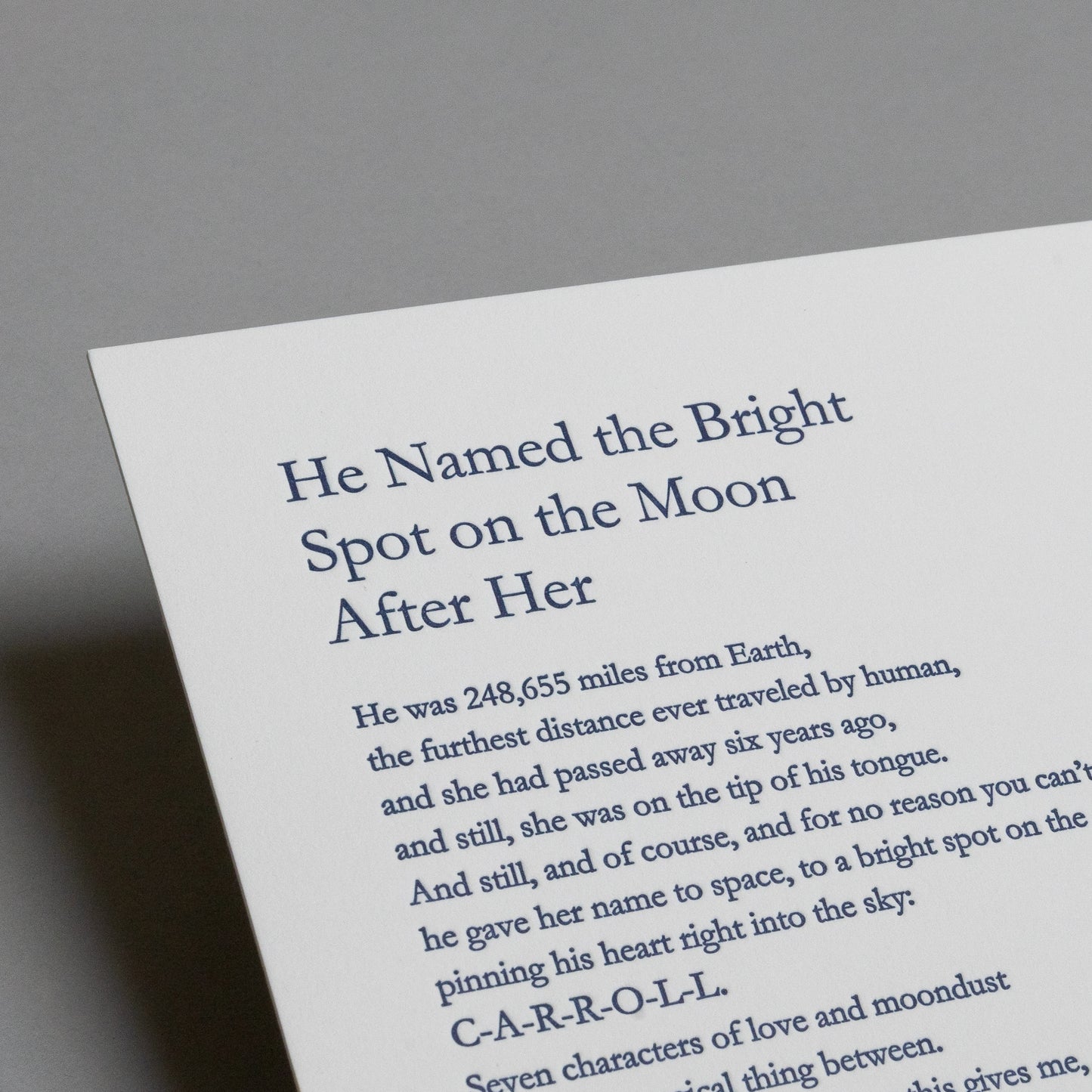 Close-up of the blue letterpress title and upper text on “He Named the Bright Spot on the Moon After Her.”