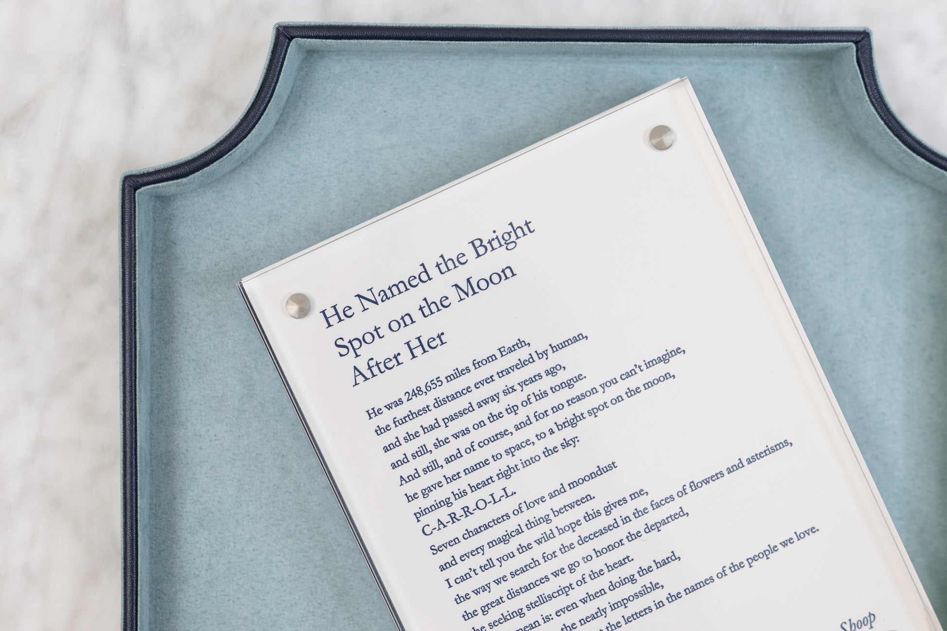 Angled detail of “He Named the Bright Spot on the Moon After Her” displayed in a clear acrylic frame on a blue-green tray.