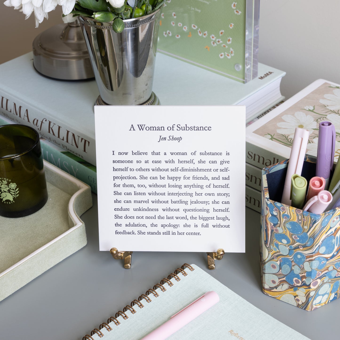 A Woman of Substance 5-by-5 poetry card by Jen Shoop displayed on a brass stand in a styled writing desk scene.