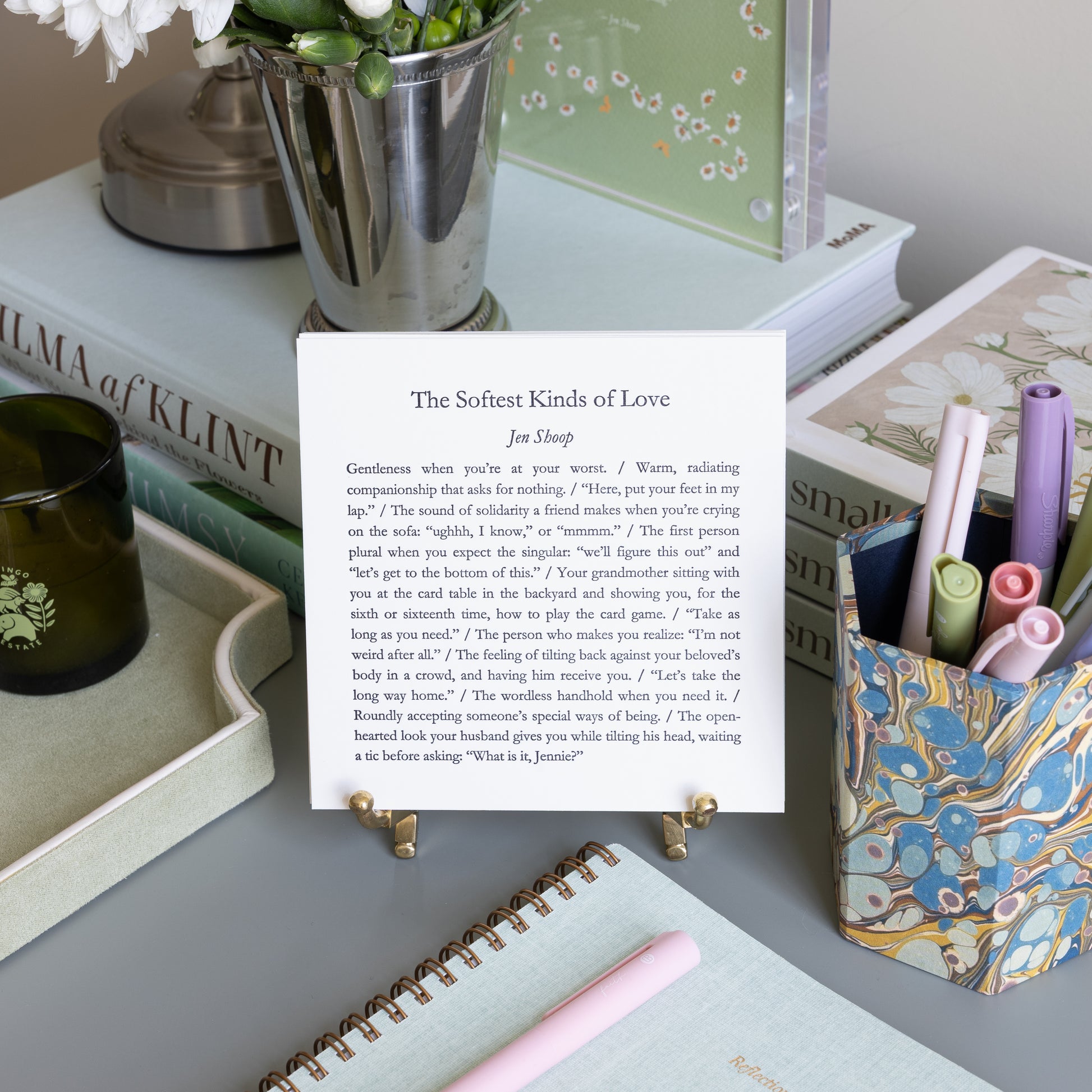 The Softest Kinds of Love 5-by-5 poetry card by Jen Shoop displayed on a brass stand in a styled writing desk scene.